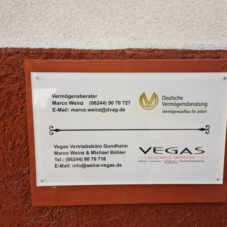 Weiße Firmtafel mit Kontaktdaten an einer rot verputzten Hauswand