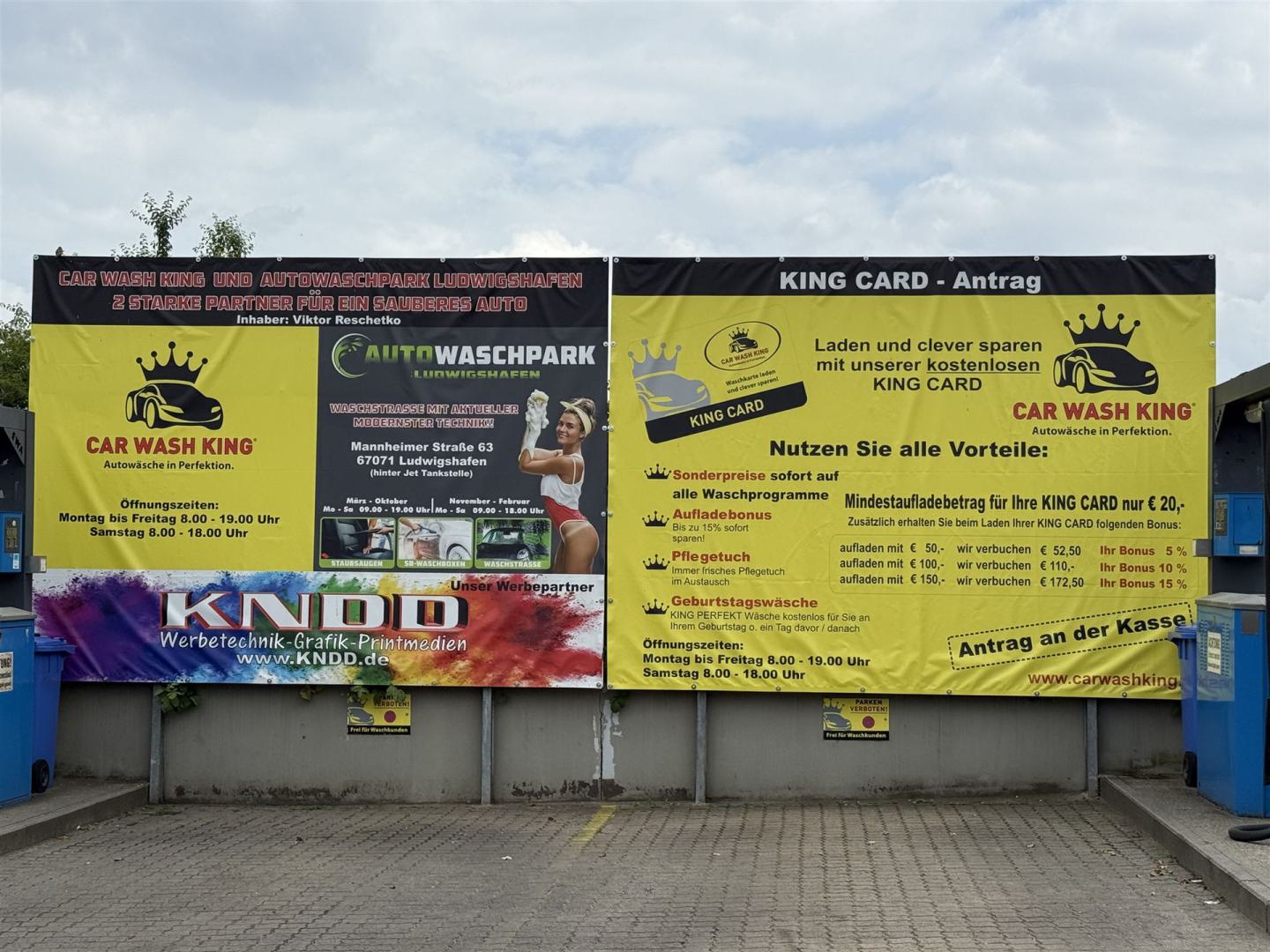Großes Werbebanner einer Autowaschanlage mit gelben und schwarzen Tafeln auf einem Parkplatz.