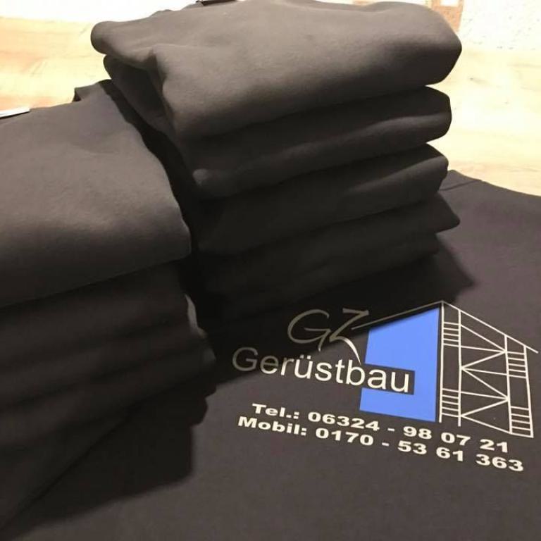 Mehrere gefaltete schwarze Kleidungsstücke mit aufgedrucktem Firmenlogo auf einem Tisch