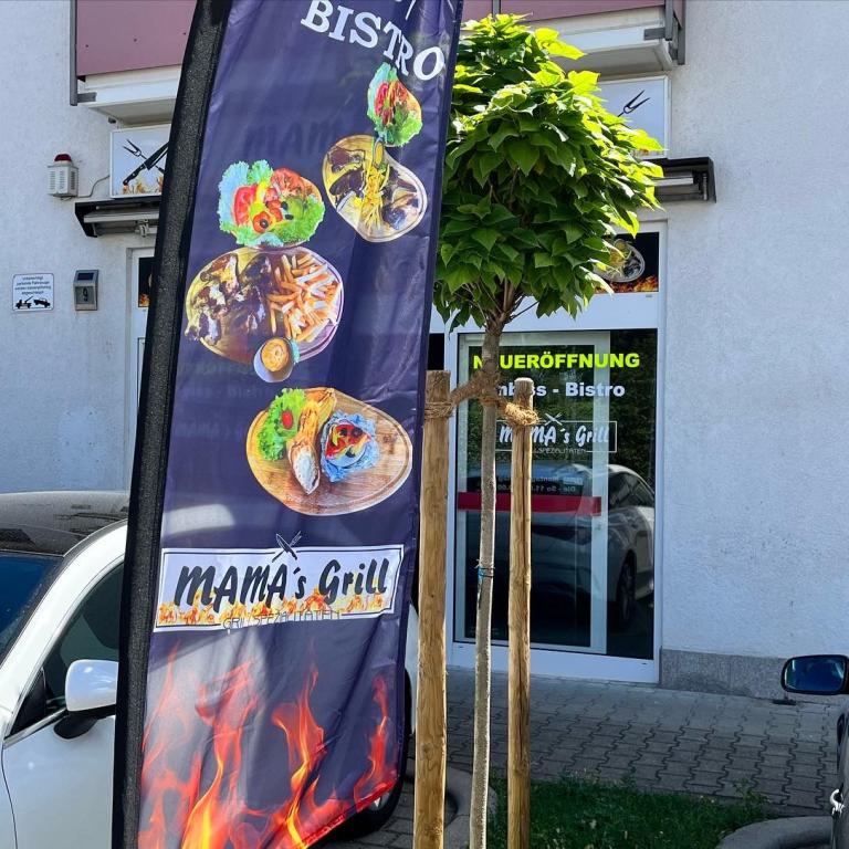 Werbefahne vor einem Bistro mit der Aufschrift MAMA's Grill vor einem Gebäude.