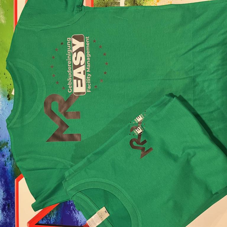 Zwei grüne T-Shirts mit Firmenlogo liegen auf einer bunten Oberfläche.