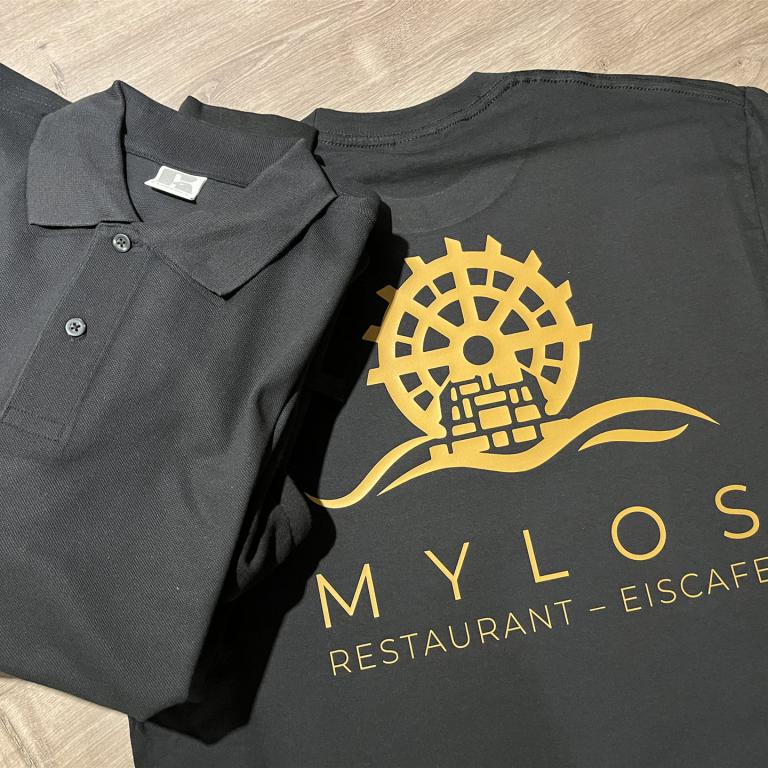 Schwarzes Poloshirt und schwarzes T-Shirt mit goldenem Mylos Restaurant Eiscafe Aufdruck.