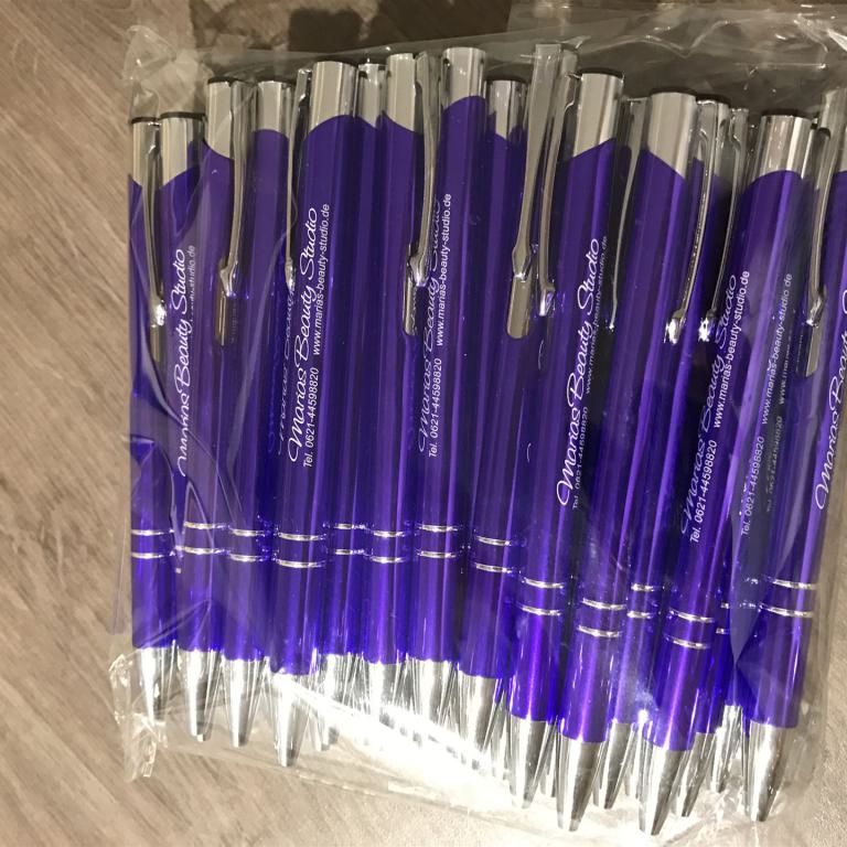 Mehrere violette Kugelschreiber mit silbernen Clips in einer transparenten Plastiktüte auf einem Holzboden.