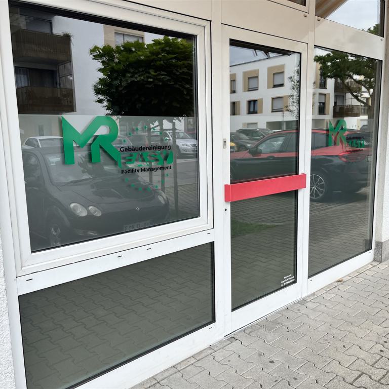 Eingangstür und Fensterfront eines Gebäudes mit Firmenlogo für Gebäudereinigung und Facility Management.