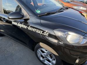 Schwarzes Auto mit der weißen Aufschrift www.daphne-devereaux.de an der Seite.