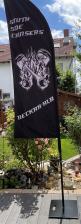 Schwarze Werbefahne mit Motorenmotiv in einem sonnigen Garten vor einem Haus