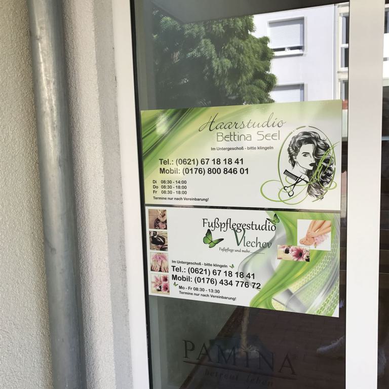 Schaufenster mit Werbeplakaten für ein Haarstudio und ein Fußpflegestudio.